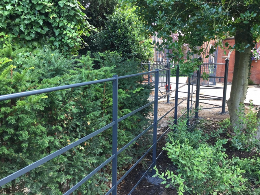 Blue-grey painted fencing forms a contrast with the plants and red brick buildings of this property